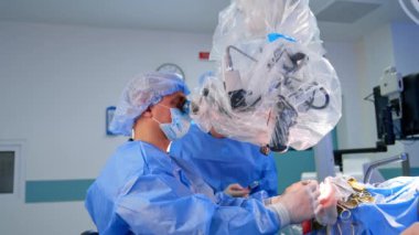 Profesyonel erkek beyin cerrahı, beyin cerrahisinde metal aletleri dikkatlice kullanır. Doktor gelişmiş mikroskoba dikkatlice bakıyor. Yan görünüm.