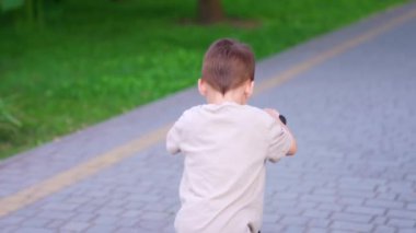 Motosiklete binen bir çocuğun arka görüntüsü. Çocuk parktaki bir şeyi parmağıyla işaret ediyor..