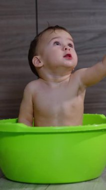 Banyo yapan sevimli çocuk bir şey için elini kaldırıyor. Lavaboda banyo yapan güzel bir bebek. Dikey video