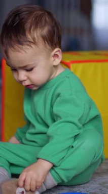 Yerde oturan bebek şişeyi düşürür ve oyuncakların dikkatini dağıtır. Hoş çocuk içeride piramitlerle oynuyor. Dikey video