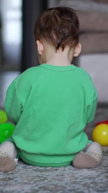 Kameraya arkasını dönmüş oyuncaklarla oynayan küçük bir çocuk. Bebek döner ve kameraya emekleyerek yaklaşır. Yanında oturan kara kedi. Dikey video