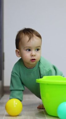 Sevimli erkek bebek topu için lavabonun etrafında sürünüyor. Kara kedi çocuğu ve kamerayı izliyor. Dikey video