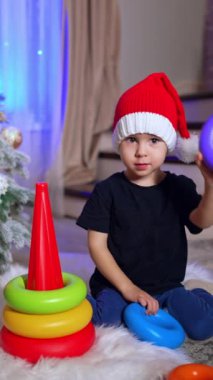 Noel Baba şapkalı iki yaşındaki çocuk piramitle oynuyor. Güzel çocuk Noel 'de evde eğleniyor. Dikey video