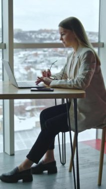 Modern ofisteki çekici yaşam tarzı kızı. Dizüstü bilgisayarla çalışan neşeli genç bir iş kadını. Dikey video