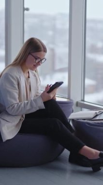 Akıllı telefonla çalışan çekici bir iş kadını. Kapalı alan kadını telefonu kullanıyor. Dikey video