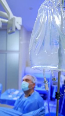 Serum askısı ve tuz çözeltisi dolu naylon poşetler. Kapatın. Cerrah ve hemşire endoskopik ameliyat yapıyorlar. Dikey video.