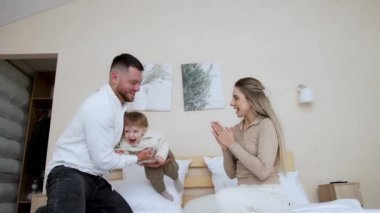 Sakallı beyaz adam küçük oğlunu kucağına alıp fırlatıyor. Mutlu sevimli çocuk sevimli bir şekilde gülüyor. Annem el çırpıyor. Düşük açı görünümü.