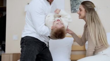 Kafkasyalı ebeveynler büyük bir yatakta oturup küçük çocuklarıyla oynuyorlar. Babası küçük oğlunu sevgiyle öpüyor. Mutlu aile fotoğrafı..