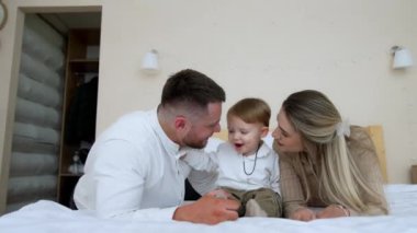 Anne ve baba yatağa uzanır ve küçük bebekleri aralarında oturur. Çocuk kaprisli olmaya başlıyor ve babasını itiyor..