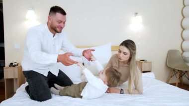 Üç kişilik aile zamanlarını yatak odasında büyük bir yatakta geçirirler. Baba, oğlunun başını eğiyor. Mutlu anne, baba ve bebek.