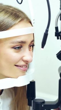 Klinikte gözlerini kontrol eden genç bir kadın. Biyomikroskopi cihazı. Modern tıbbi ekipmanların yardımıyla bir kadın hastanın göz yapısını inceleyen bir doktor. Profesyonel sağlık hizmeti. Dikey video