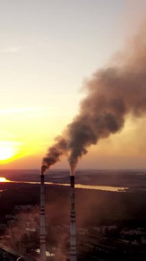 Gün batımında sanayi fabrikası. Akşamları arka plandaki borulardan dumanlar yükseliyor. Nehir kenarında üretim. Dikey video