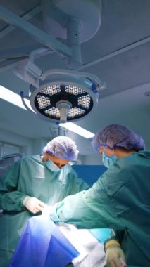 İki kadın doktor ameliyat yapıyor. Cerrah metal aletleri uygular ve hemşire de cerrahi bölümünden sünger alır. Dikey video.
