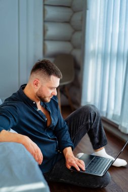 Modern kapalı mekanlarda dizüstü bilgisayarda çalışan bir adam. Bir adam yerde oturuyor, dizüstü bilgisayarıyla meşgul, şık dekorlu, aydınlık bir odada..