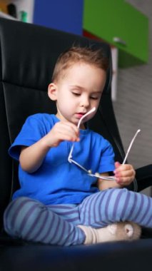 Güneş gözlüklü komik çocuk oynuyor. Deri sandalyede oturan küçük çocuk. Dikey video