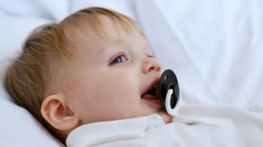 Yastığın üzerinde beyaz saçlı, tatlı beyaz bir erkek bebek yatıyor. Emziği olan çocuk uykuya dalıyor. Kapat..