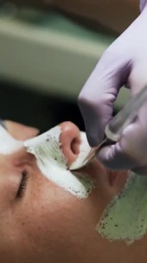Beyaz maskeli beyaz bir kadının yüzünü kapatıyordu. Güzellik salonunda kozmetoloji prosedürleri. Kapatın. Dikey video
