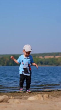 Güneşli bir günde yaz oyunu. Kumsalda oynayan küçük bir çocuk. Dikey video