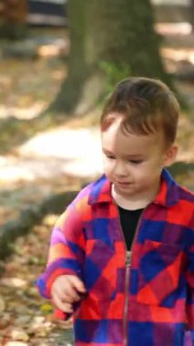 Çizgili kumaş giyen çocuk oynuyor. Küçük şık bir çocuk dışarıda yürüyor. Dikey video