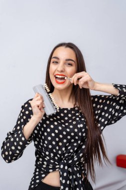 Puantiyeli gömlek, diş bakımı. Uzun saçlı bir kadın elinde diş fırçası ve diş kiti tutarken gülümsüyor. Ağız hijyenine olan sevgisini gösteriyor..