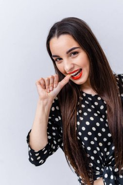 Kadın parmağını ısırıyor, benekli. Uzun saçlı genç bir kadın, şakacı bir şekilde parmağını ısırırken gülümsüyor, açık arka planda benekli bir bluz giyiyor..