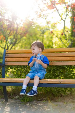 Çocuk güneşli park gününün tadını çıkarıyor. Çocuk elinde bir su şişesiyle parkta oturuyor güneşli bir öğleden sonranın tadını çıkarıyor..