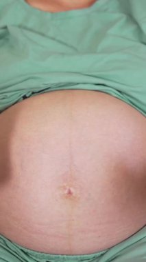 Müstakbel annenin karnına çorap ördüm. Hamile kadın kanepede yatıyor ve göbeğinde küçük mavi çoraplar gösteriyor. Ön manzara. Dikey video