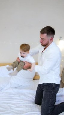 Güçlü beyaz adam küçük bebeğini sağa sola sallıyor. Önemseyen baba oğluyla evde oynuyor. Dikey video.