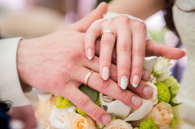 Çiftler alyans takar. Alyanslarla süslenmiş iki el neşeli bir düğün kutlaması sırasında bir buket çiçeğin üzerinde dinleniyor..