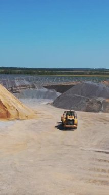 Taş ocağındaki kazıcı. Asfalt fabrikasının büyük bir bölgesi. Dışarıda kum ve enkaz yığını var. Hava görüntüsü. Kamera hareketi yukarı. Dikey video