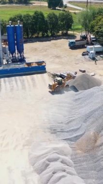 Yukarıdan asfalt bitkisi. Kazıcı dışarıdaki yığının üzerine harabeler döker. Doğayla çevrili asfalt fabrikasının modern toprakları. Dikey video