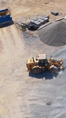 Buldozerli asfalt fabrikası. Fabrika yol inşaatının ihtiyaçlarına hizmet ediyor. Endüstriyel makine enkazları yüklüyor. Hava görüntüsü. Dikey video