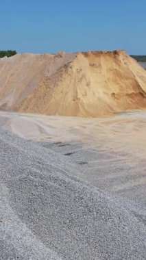 Dışarıda ezilmiş taş ve kum yığınları var. Buldozer güneşli bir günde asfalt fabrikasında çalışıyor. Hava görüntüsü. Dikey video