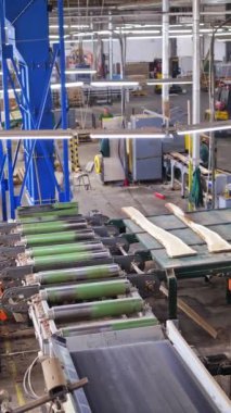 İçerideki ahşap fabrikası. İşçiler tahtaları otomatik ekipmanlarla yapma sürecini kontrol ediyorlar. Elektrikli testere tezgahı. Dikey video
