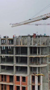 Şehirde yeni bir inşaat alanı. Şehir binasını inşa eden iki büyük vinç. Şehrin arka planında yüksek binalar inşa ediliyor. Hava görüntüsü. Kameranın yuvarlak hareketi. Dikey video