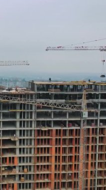 Şehir merkezinde yeni inşaat. Açık havada inşaat halindeki yüksek katlı bina. Hava görüntüsü. Kamera hareket ediyor. Dikey video
