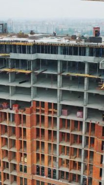 İnşaat alanında büyük bir konut. Şehir manzaralı yeni gelişmelerin insansız hava görüntüsü. Arkasında şehir olan yeni bir binanın geniş görüşü. Dikey video