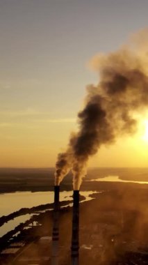 Gün batımında yoğun dumanlı endüstriyel borular. İki büyük boru doğanın arka planında kimyasal duman üretir. Çevre kirliliği. Dikey video