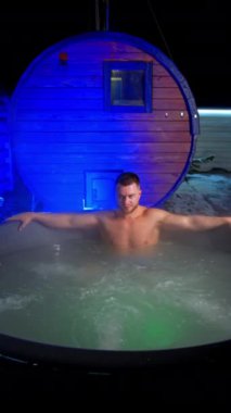 Genç adam jakuzide oturur ve elleri küvetin kenarına yayılır. Rahatlama ve spa prosedürleri. Dikey video.