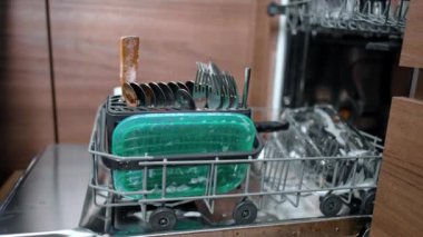 Sabunla kaplı bulaşık ve mutfak aletleri bulaşık makinesine konur. Kadın eli bıçağı saplar ve makineyi kapatır..