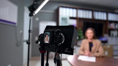 Ofiste günlük içeriği oluşturma. Bej ceketli bir kadın profesyonel kamerada bir video kaydediyor. Bulanık arkaplan.