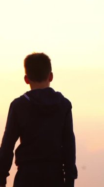 Çocuk gün batımında sahilde yürüyor. Çocuk sahilde gün batımında tek başına yürüyor.