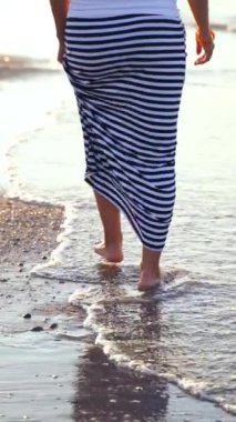 Deniz kıyısında yürüyen bir kadın. Güzel, genç, çıplak ayaklı bir kadın deniz dalgalarında yürüyor.