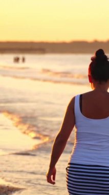 Sahilde yürüyen yalnız bir kadın. Arka portre kızı deniz sahilinde şık bir kıyafetle yürüyor.