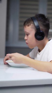 Genç çocuk mutfakta yemek yiyor. Çocuk tablette yemek yiyor ve çizgi film seyrediyor.