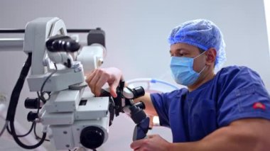 Profesyonel cerrah modern mikroskopta duruyor. Sıhhiye ekipmana bir dürbün takıyor. Düşük açı. Nöroşirürji için hazırlık.