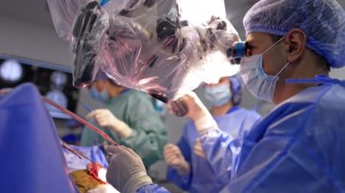 Mikroskopta oturan profesyonel beyin cerrahı kan emici bir alet kullanıyor. Asistanlar enstrümanı doktora verir..