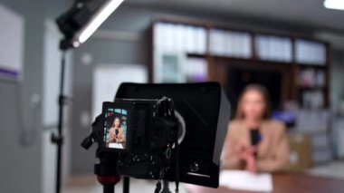 Kamerada bej ceketli beyaz kadın konuştu. Blogcu bulanık arkaplanda oturmuş kamerayla konuşuyor.