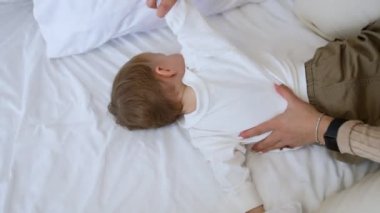 Sarışın kadın küçük oğluna masaj yapıyor. Babam izlemenin yanında oturuyor. Üçüncü kattaki aile tuvalette. Yüksek açı görünümü.