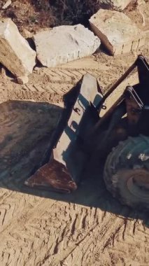 Özellikle teçhizatlı buldozer, taş ocağında ormanlı bir kayanın arka planında bir taş topluyor. Kum ocağının manzarası. Kamera yukarı, dikey video.